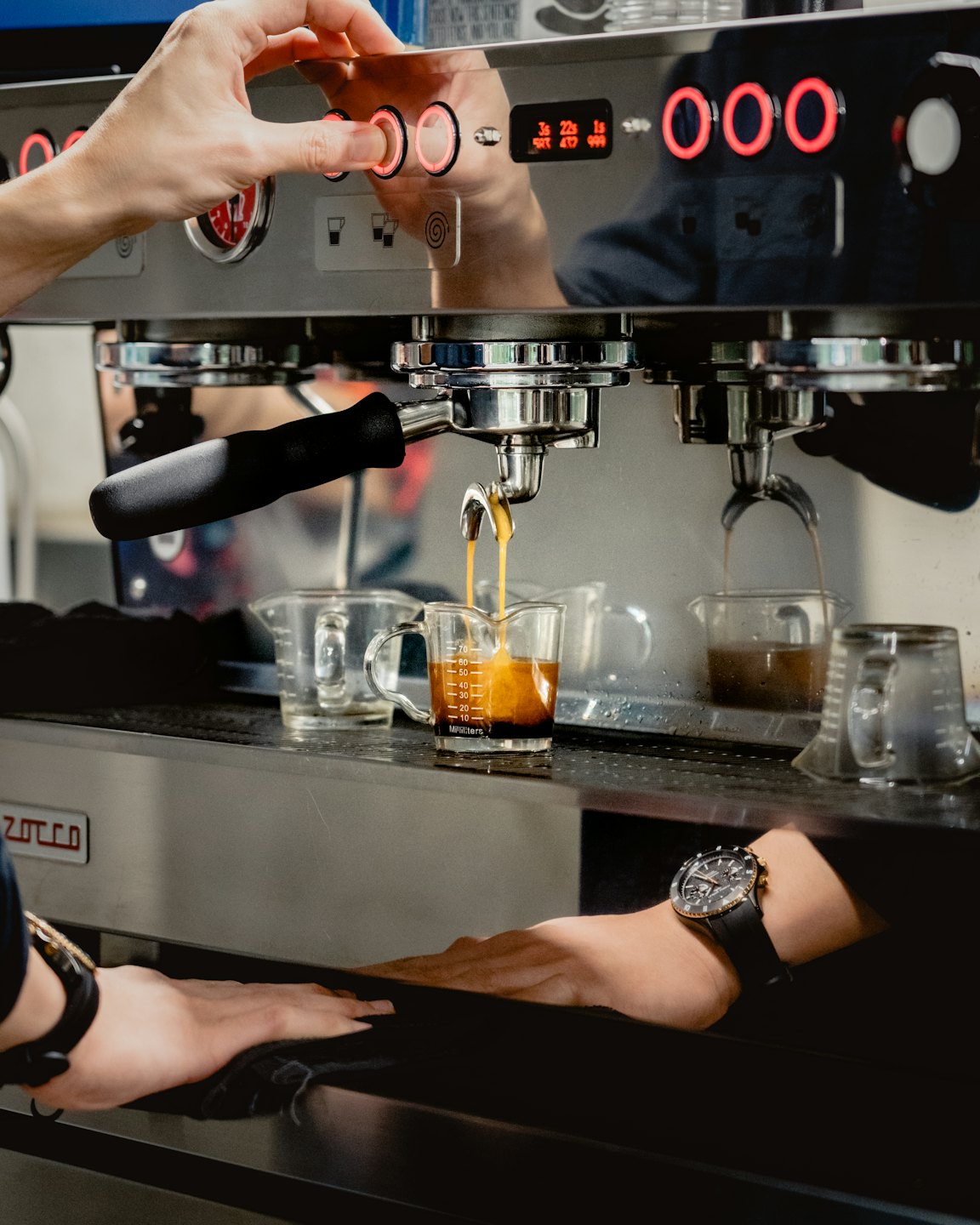 Hände bedienen eine Edelstahl-Espressomaschine und brühen frischen Kaffee.