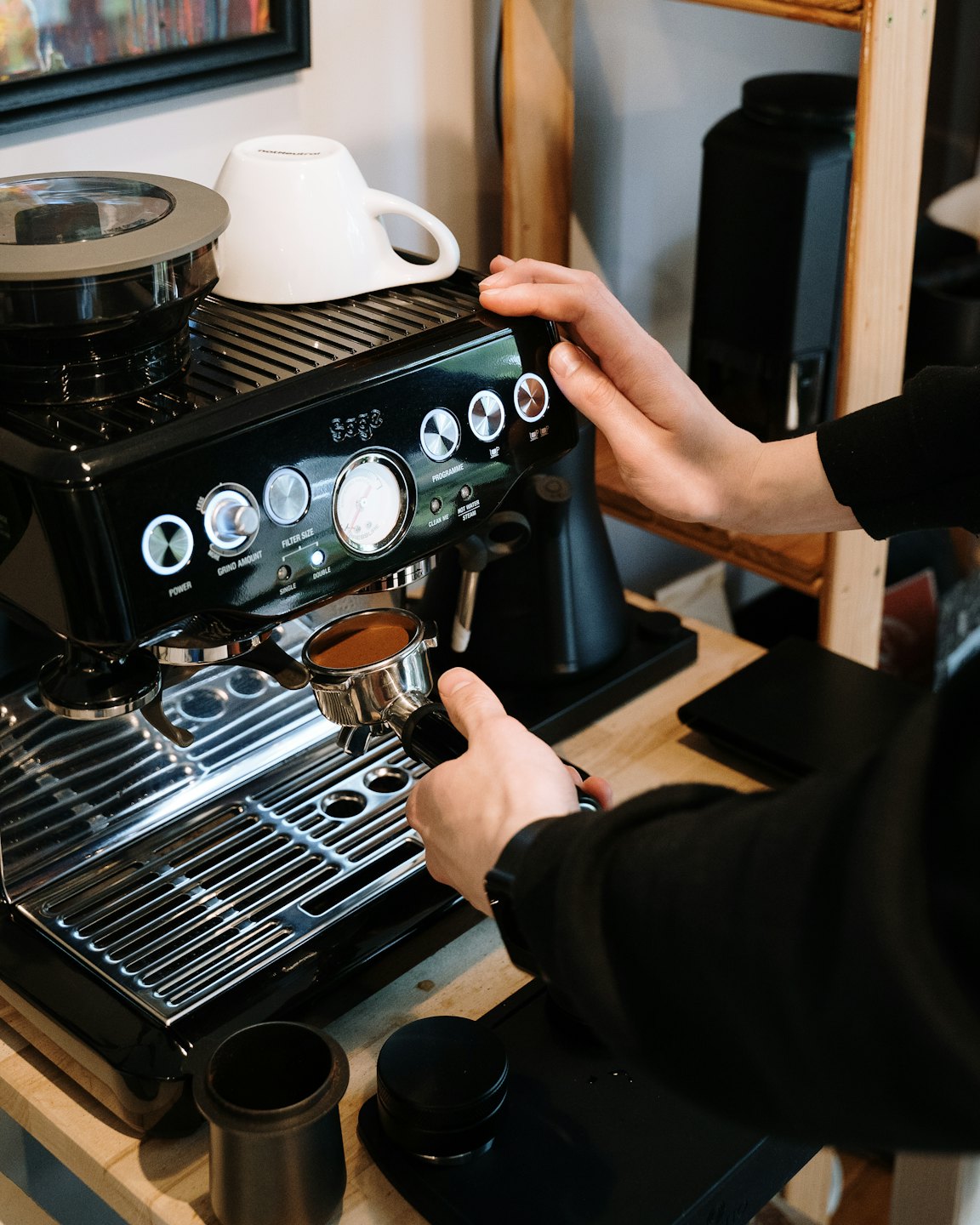 Hände bedienen eine Espressomaschine und bereiten Kaffee auf einer Theke zu.